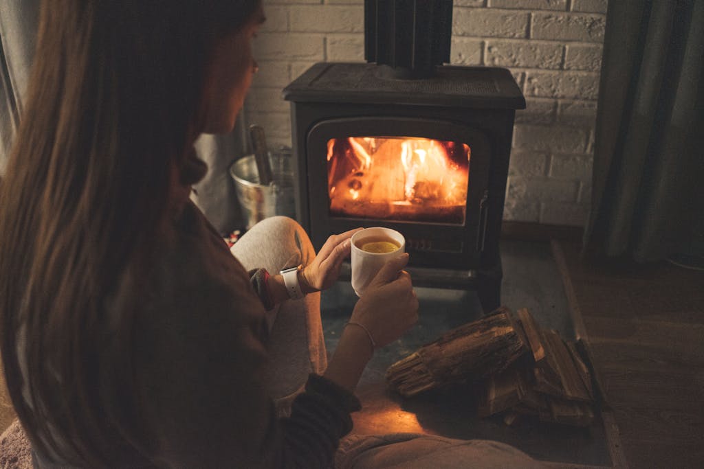 A woman enjoys a warm cup of tea by the fireplace, creating a cozy atmosphere indoors.